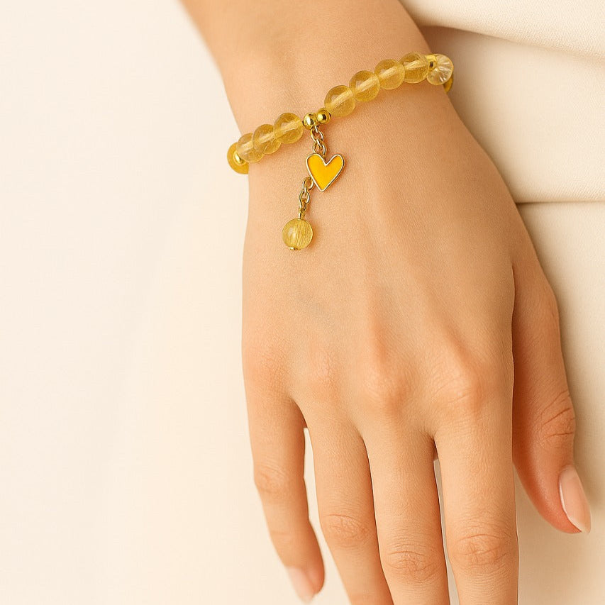 Hand wearing a yellow beaded bracelet with heart charm on a beige background