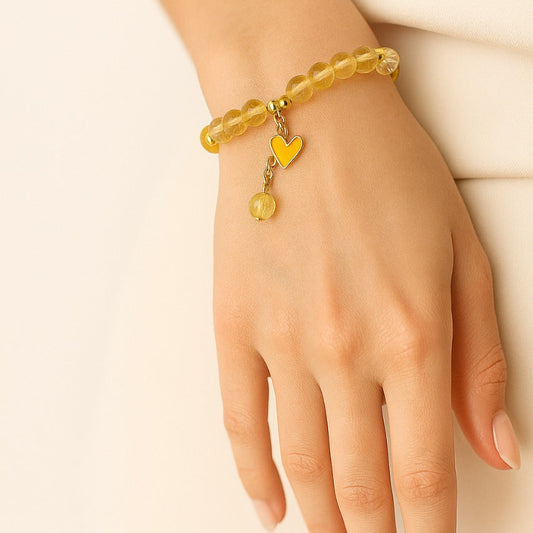Hand wearing a yellow beaded bracelet with heart charm on a beige background